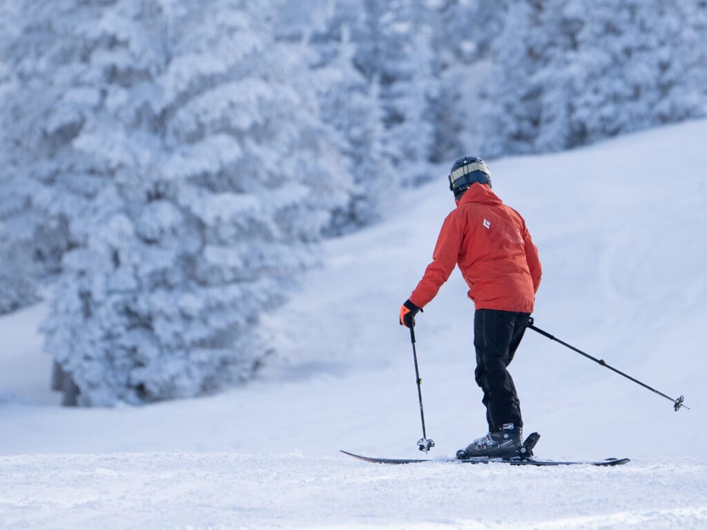 A skier with poles skis on the slopes of Snowbowl, Flagstaff, AZ with trees nearby.