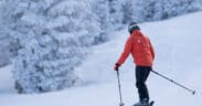 A skier with poles skis on the slopes of Snowbowl, Flagstaff, AZ with trees nearby.