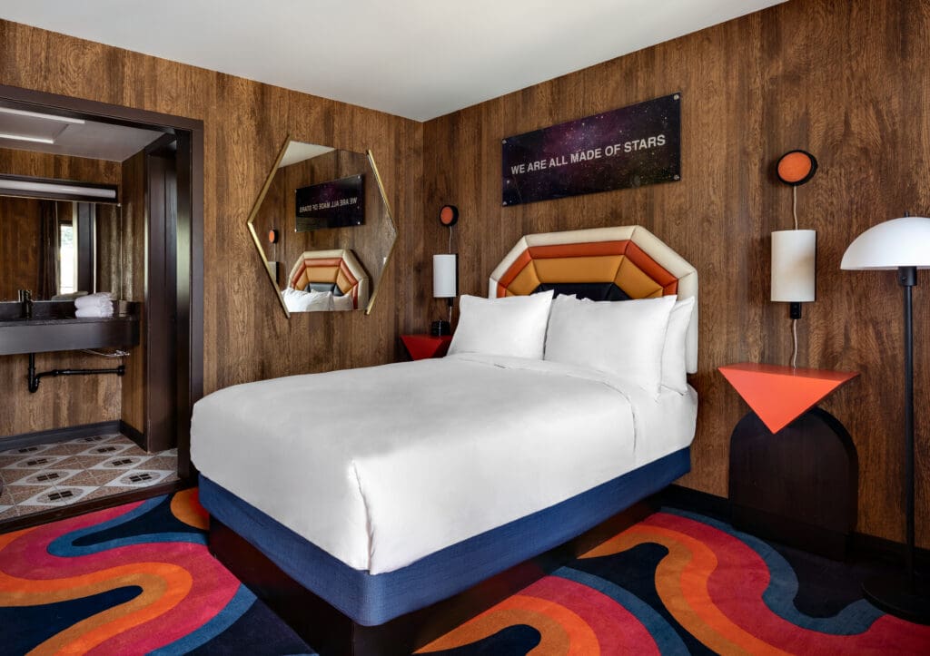 Guest room with a queen-size bed and funky swirly carpet and 70's retro decor with open access to the bathroom at at The Americana Motor Hotel in Flagstaff.