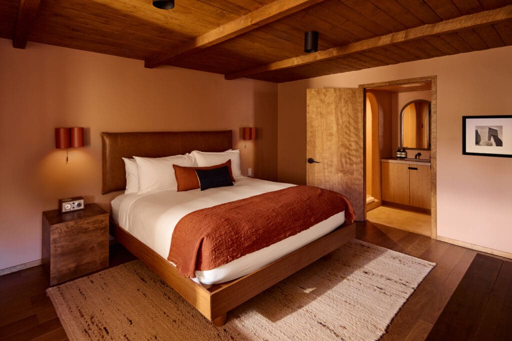 A refreshed guestroom at Hotel Willa with a king bed, dresser and woven rug with a high-beam ceiling.