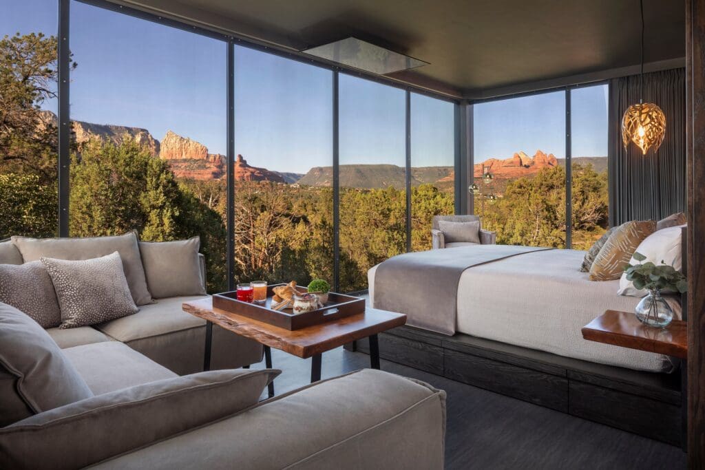 The inside of an Ambiente atrium with a comfortable bed, sofa, table with charcuterie snacks and windows looking out to the Sedona Red Rocks.