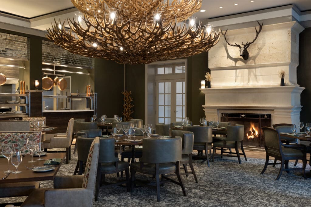 A set up of luxury tables and chairs at the Photo courtesy of Antlers Lodge at Hyatt Regency Hill Country Resort's Antlers Lodge fine dining restaurant with deer antlers above the fire place.