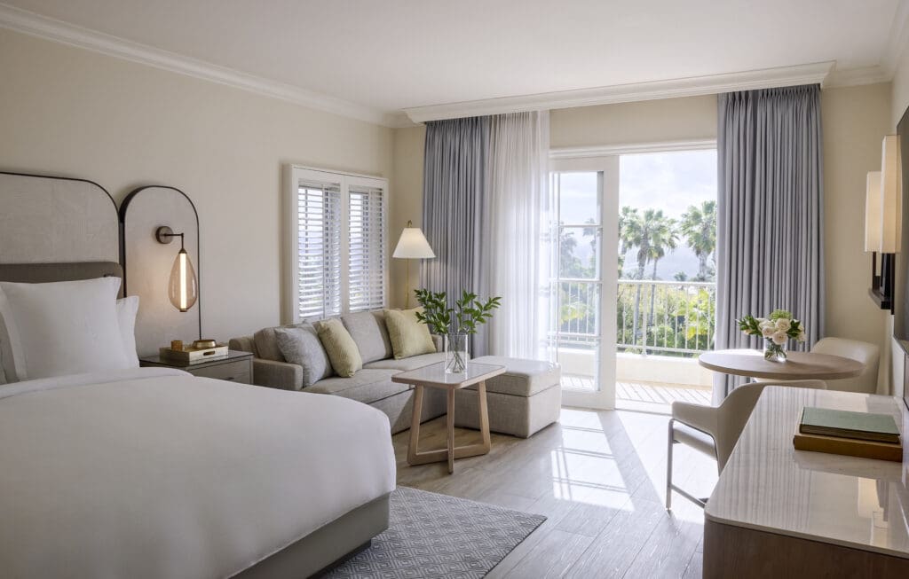 A newly renovated guestroom at Four Seasons Residence Club Aviara with an immaculately made bed, small sofa and a balcony overlooking the San Diego coast.