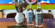 Creative Spirits liquor bottles are on a table next to paintbrushes in a vase at Weft & Warp.
