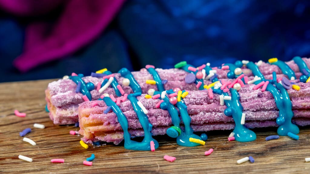 Two Disneyland Resort 70th Celebration Churros rolled in ube sugar and topped with marbled blue raspberry icing drizzle and sprinkles.