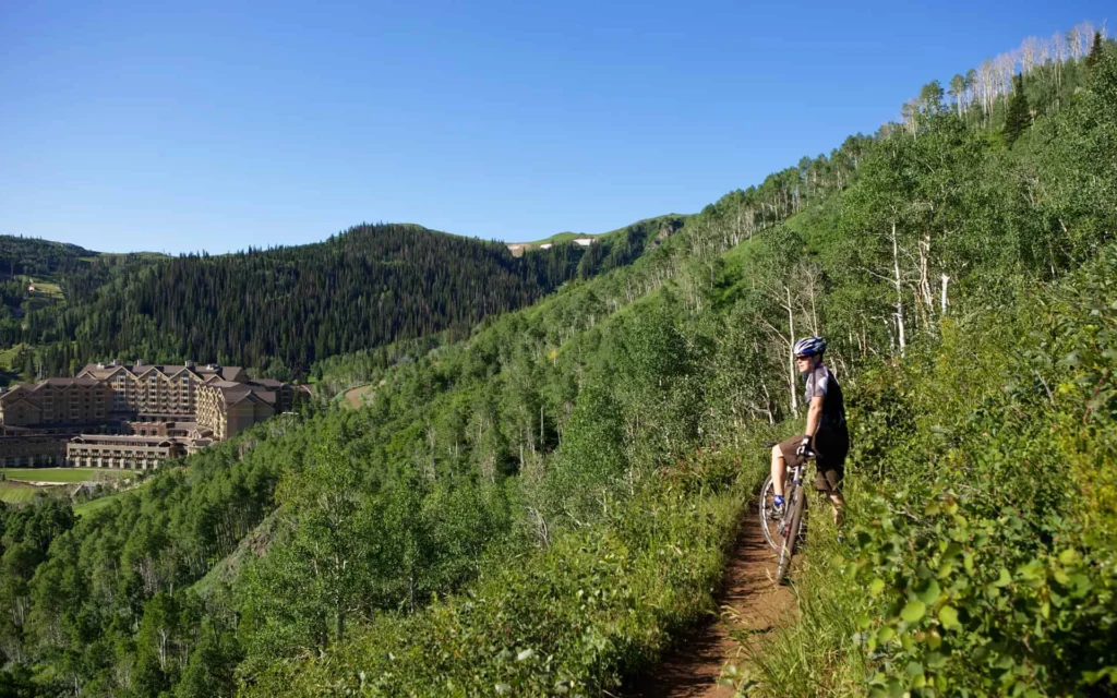 One of the 400-plus bike trails by Montage Deer Valley, with a biker on his bike overlooking the valley, surrounded by trees.