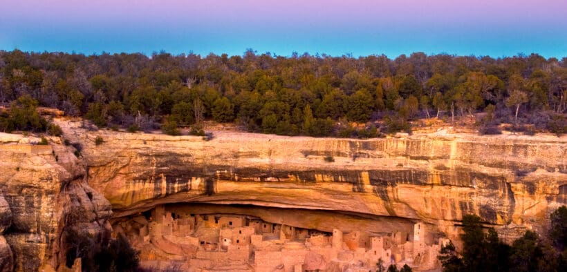 A photo of Mesa Verde National Park cliffs and canyon topped with trees.