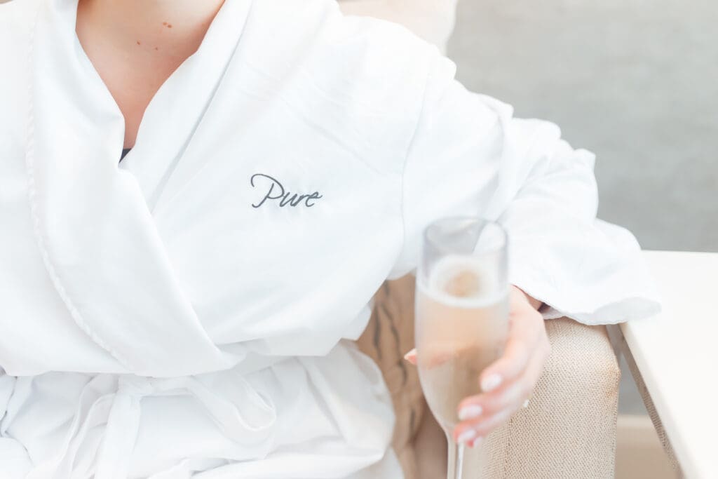 A woman is in a robe embroidered with "Pure" as part of promoting the Marriott Marquis Houston Mother's Day spa offerings.