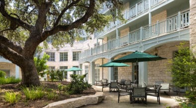The Springhouse Cafe with outdoor umbrellas outside of the Hyatt Regency Hill Country Resort with large tree and landscaping