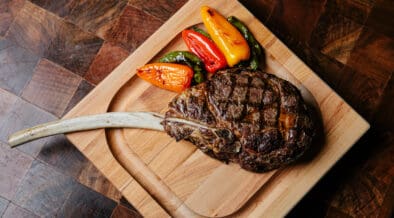 A Tomahawk steak and peppers on a cutting board at J&G Steakhouse at The Phoenician