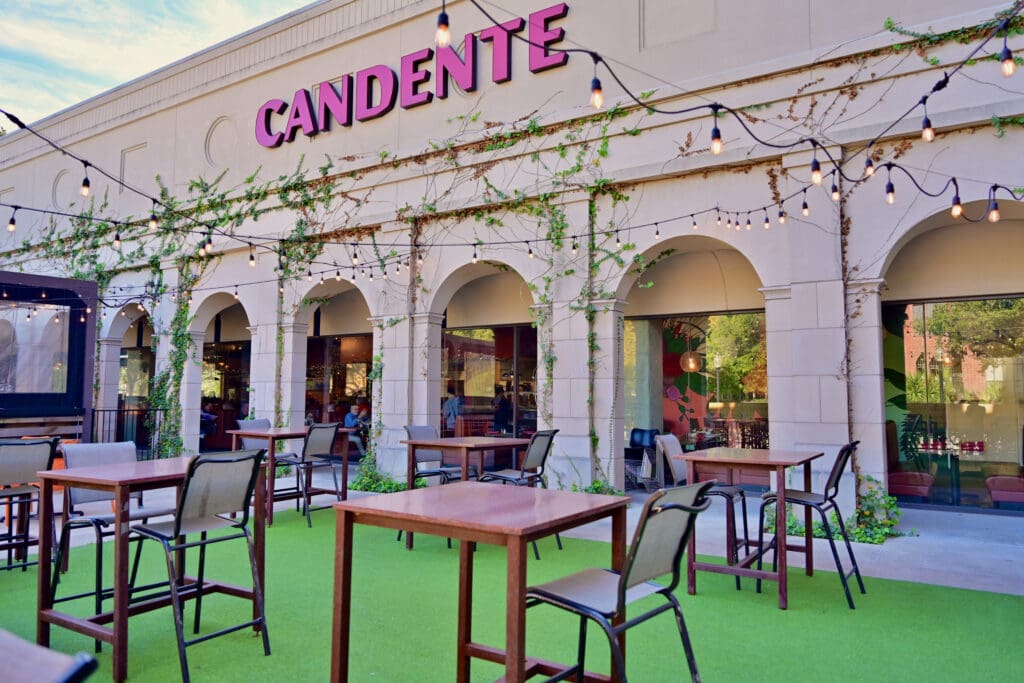 The outdoor of Cadente with string lights and bistro style seating with chairs on green turf outside.