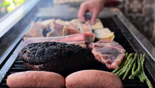 Two sweet potatoes, asparagus, steak and ribs are on the grill.