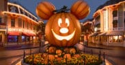 A big lit up pumpkin head of Mickey Mouse in the center of Main Street Disneyland surrounded by lit up shops.