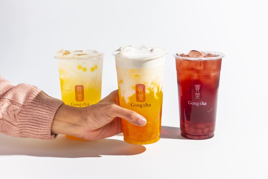 A person's hand grabs for one out of three lined up Gong cha iced drinks.