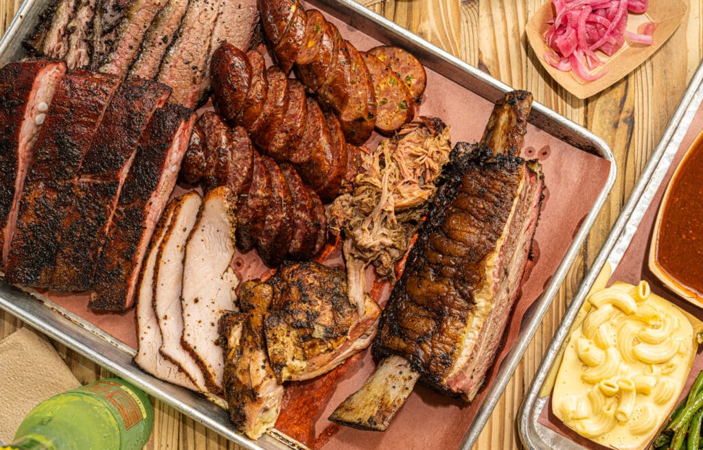 The Pit Room's slab of various meats: brisket, ribs, sausage, plus mac 'n cheese and more on a table.