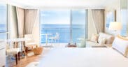 A king-size bed, a couch, a table and two chairs with glass-front windows at Surf & Sand, Laguna Beach looking out to Laguna Beach.