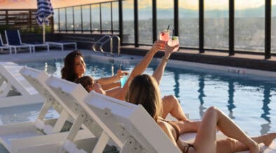 Two women in Adorandak chairs toast each other with cocktails on the Rose & Thorn restaurant atop the Penrose.