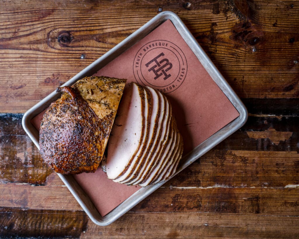 TRUTH BBQ's sliced turkey on a tray sitting on a wood table.