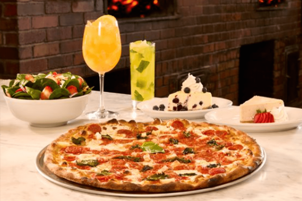 A Grimaldi's Margherita pizza next to two cheesecake plates, strawberry salad and cocktails.