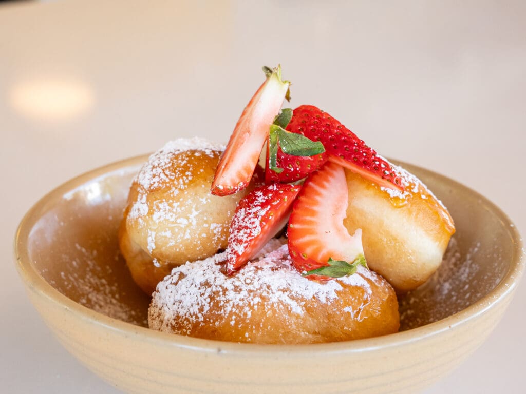 A bowl of Brown Butter Beignets from Over Easy topped with fresh-cut strawberries.