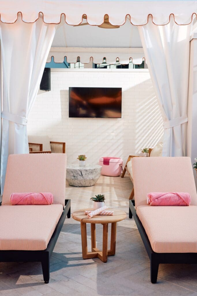 Two lounge chairs with towels are separated by a coffee table in a poolside cabana for Club Soliel at The Global Ambassador.