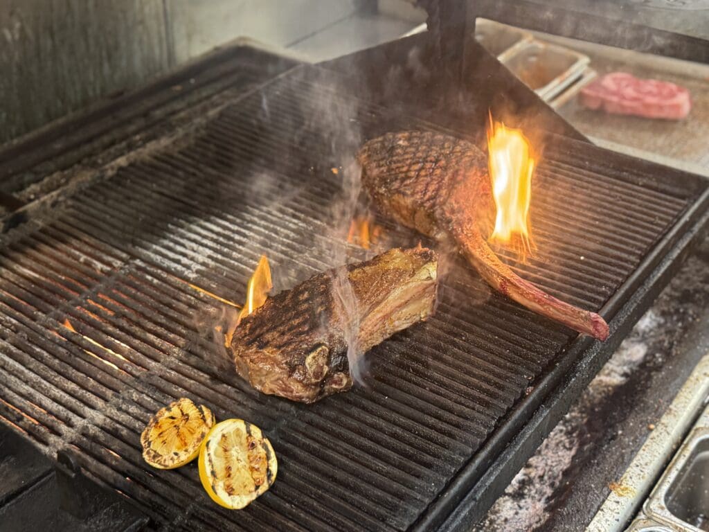 Two ribeye steaks and two lemon wedges cook on an outdoor grill at ChoP Chandler.