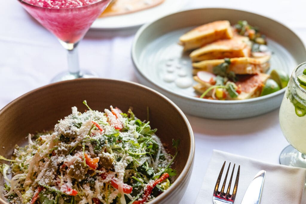 Two bowls with summer dishes and a cocktail on a table at Elvira's at DC Ranch.