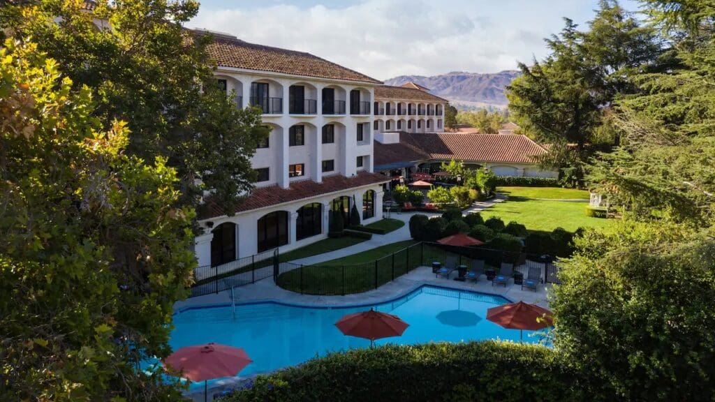 A pool with umbrellas and seating areas surrounded by lush trees and rooms at the Hyatt Regency Westlake in California.