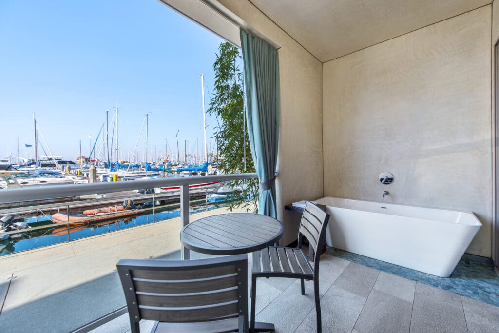 A balcony marina-view guestroom at Shade at the Marina in Redondo Beach with a soaking tub, bistro table and two chairs.