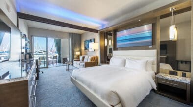 A Shade at the Marina Redondo Beach Deluxe King room with comfy bed, dresser, couch and balcony views of the marina.