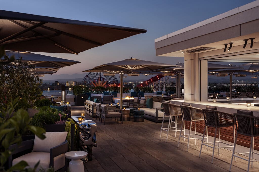 The RISE Rooftop Lounge at The Westin Anaheim Resort with rooftop seating under umbrellas with DIsneyland Resort in the background.