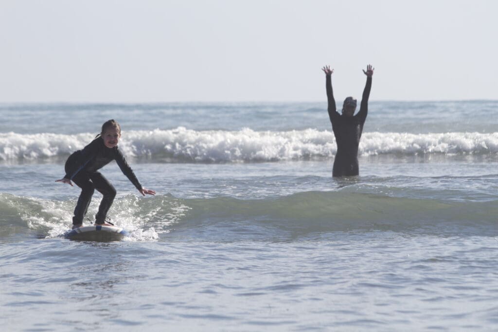 A father looks on as his daughter catches a wave taking lesons with CoreysWave in Montauk, New York.