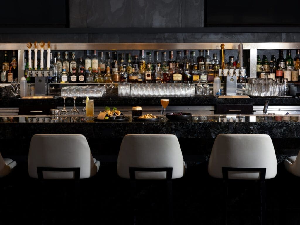 The Four Seasons Hotel Denver, EDGE Restaurant and Bar's bar lined with alcohol bottles and three cushy bar chairs.