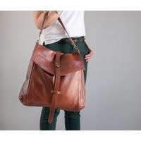 A woman in a white t-shirt and jeans carries a LeatherDesignStudio Convertible Carryall.