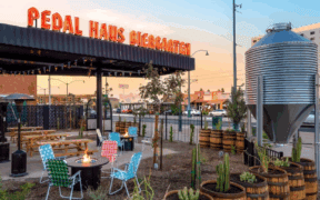 The outdoor view of Pedal Haus Brewery in Mesa with seating, a firepit and decorative barrels with plants.
