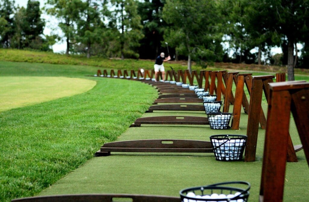 A driving range at Pelican Hill Golf Club at Laguna Beach with baskets of golf balls and a man practicing golf.