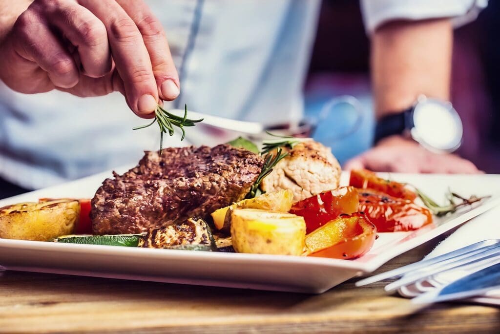 A plate of steak and grilled veggies with a chef in the background at Ruth's Chris Steak House, Hotel Park City.