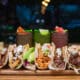 A plate of different types of tacos at Salt + Lime Modern Mexican Grill in Arcadia with three cocktails in the background.