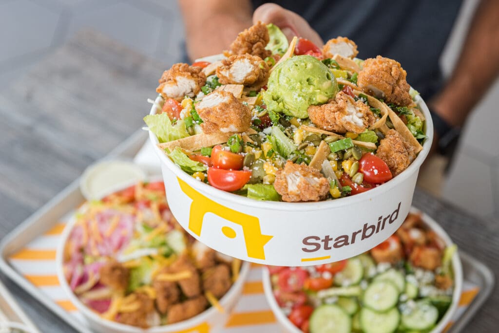 A to-go bowl of Starbird chicken salad with chicken strips, tortilla strips, tomatoes and corn.