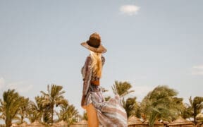Rear view of stylish blonde Woman in boho resort summer dress and sun hat.