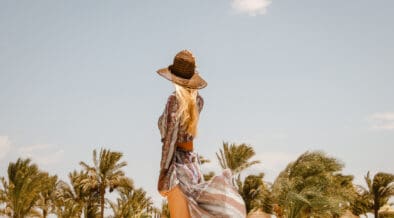 Rear view of stylish blonde Woman in boho resort summer dress and sun hat.