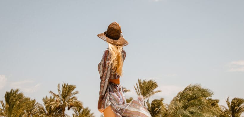 Rear view of stylish blonde Woman in boho resort summer dress and sun hat.