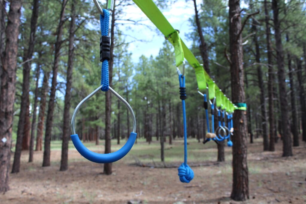 Varying strength exercise equipment hangs from a reinforced rope between trees in The Barefoot Trail in Flagstaff.