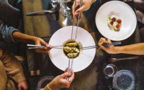 Group of people sharing Chinese steamed dumpling, view of the table with four hands holding chopsticks on fusion food luxury restaurant.