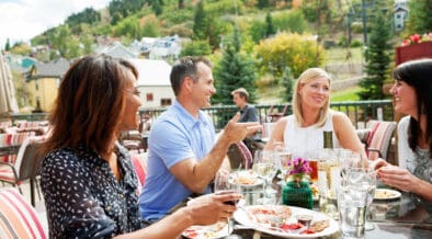 A group of people sit at an outdoor dining spot in Park City with a view of the surrounding mountains.