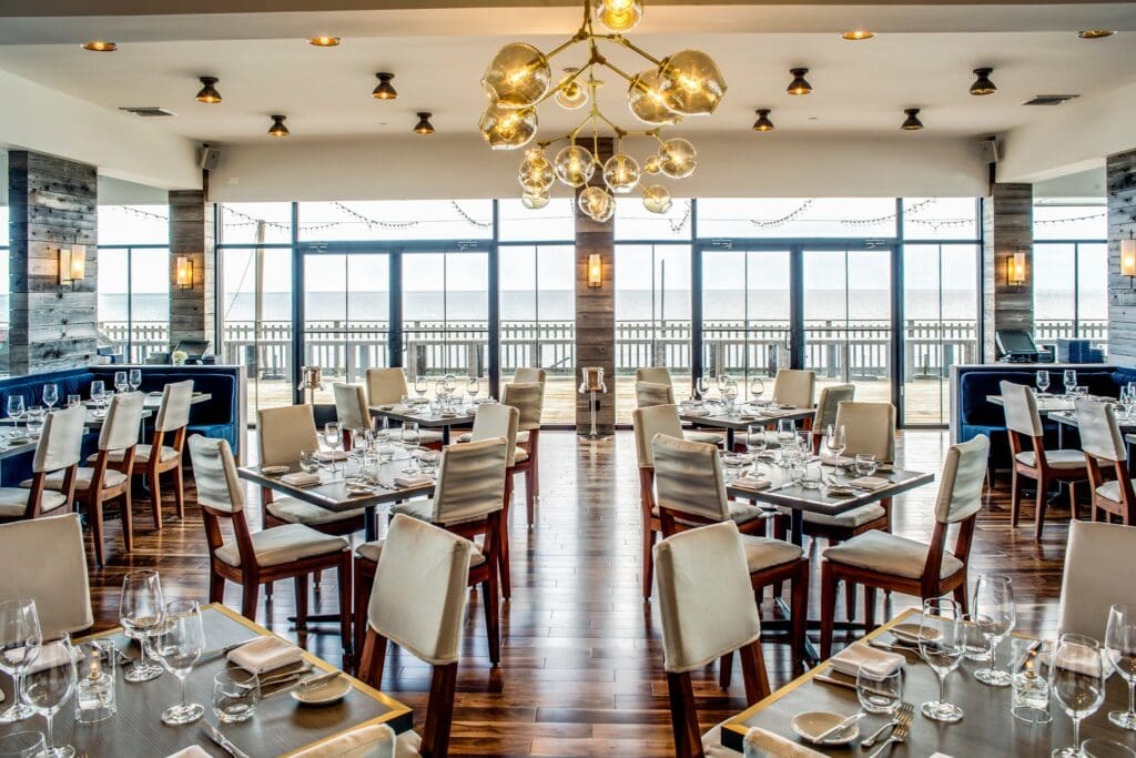 Tables, chairs and modern lighting with a view of the ocean at Scarpetta at Gurney’s Montauk Resort & Seawater Spa. 