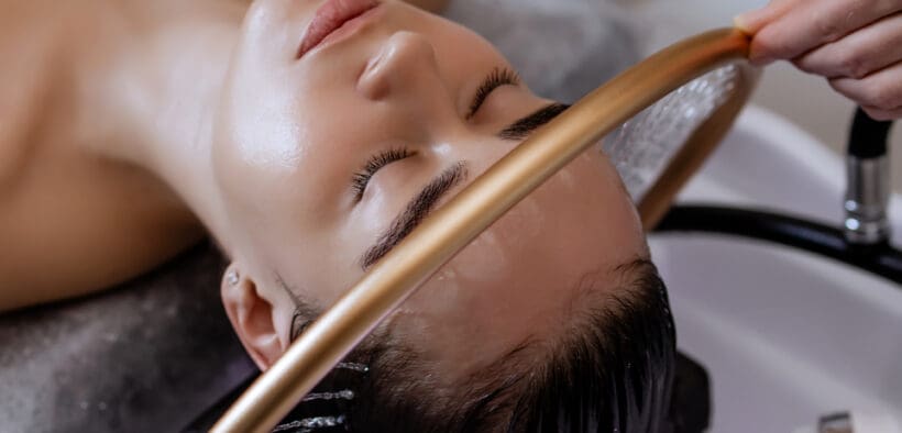Close-up of a woman receiving a head massage during a Japanese head spa treatment with water flowing from a special hair washing tool, focusing on the scalp.