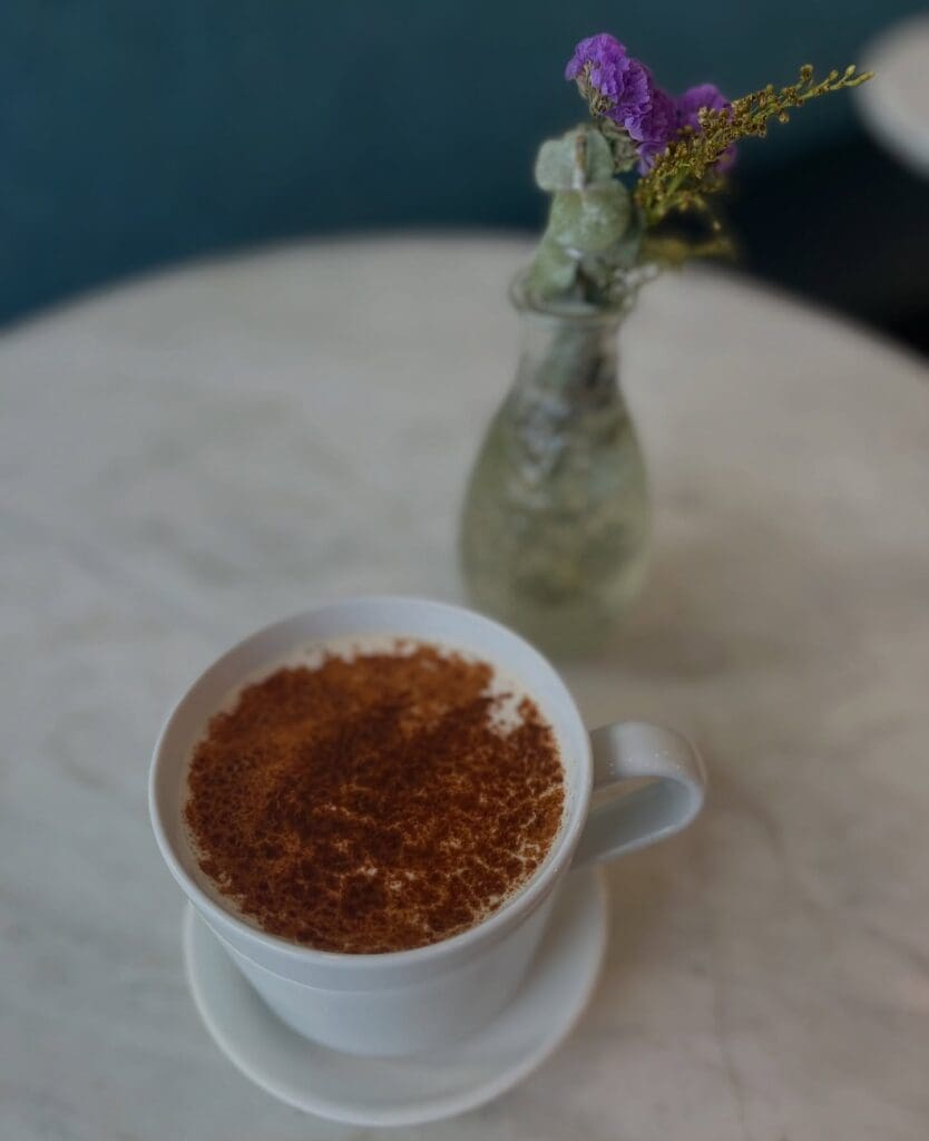 A coffee mug full of pumpkin pie latte, topped with cinnamon next to a vase with a purple flower at D Bar in Denver.