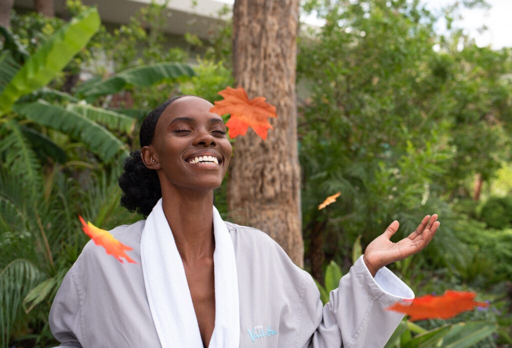 A smiling woman in a robe tosses fall leaves into the air at Hotel Valley Ho.