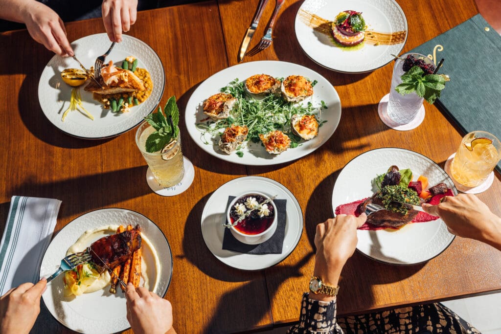 A group of people gather in front of several savory and sweet dishes, with beverages, at Jots restaurant at The Gunter Hotel.
